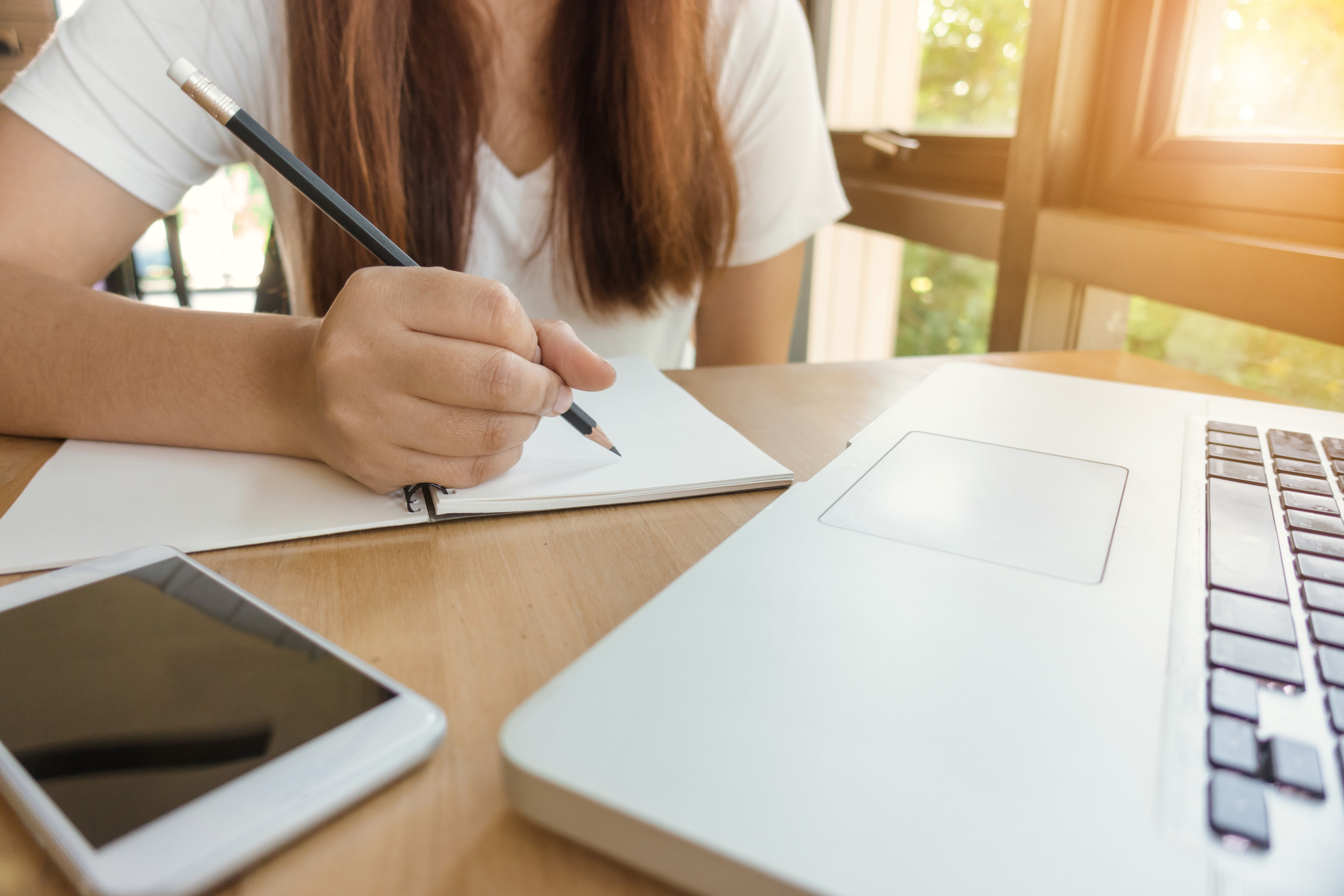 A student takes notes with a pencil with a laptop and cell phone in front of her